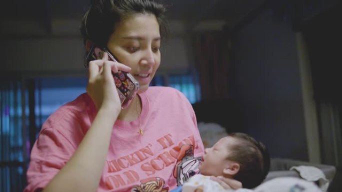 亚洲妈妈在电话上工作，抱着正在睡觉的男婴。