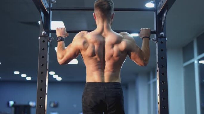 英俊的强壮的运动员的男子泵起来的背部肌肉。健身男在健身房的横木上裸着做引体向上。健身健身和健美概念。
