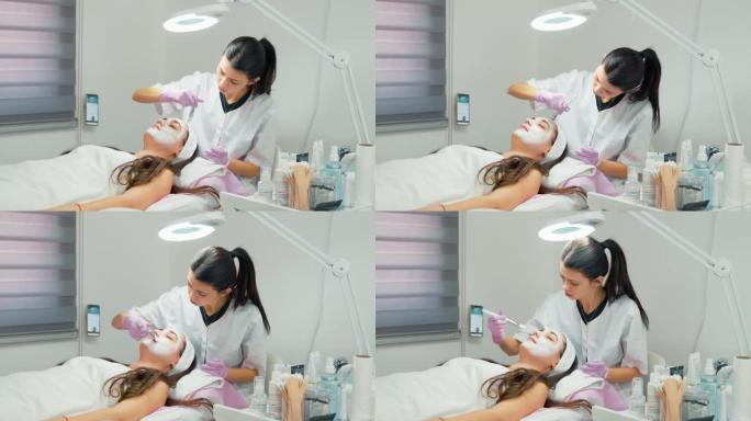 女性-客户与美容师交谈，而医生用特殊的皮肤乳霜混合物涂抹客户的脸，在医疗办公室使用刷子