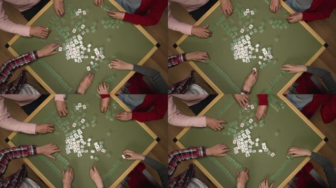 四个人的手的俯视图，在麻将桌上用绿色的白色瓷砖构成堆叠的墙壁，同时在农历新年在家享受室内娱乐
