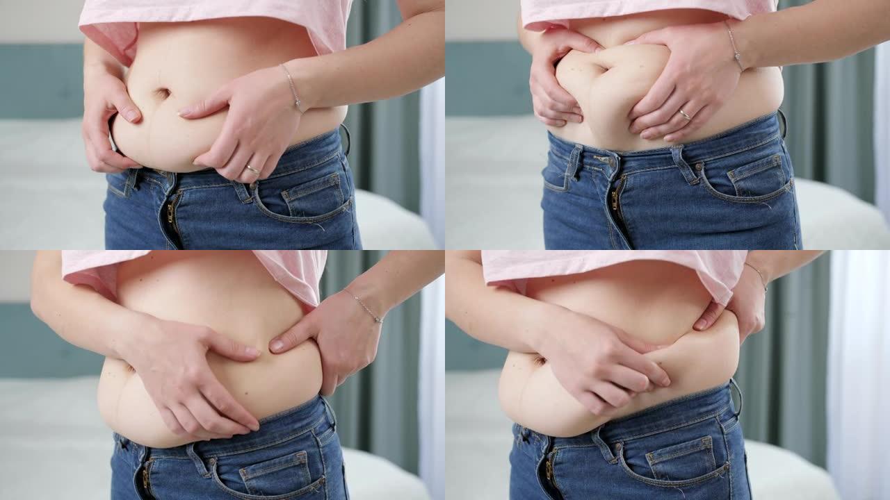 年轻女子摸着她的大肚子，拿着脂肪褶皱。超重、肥胖女性、节食和超重问题的概念
