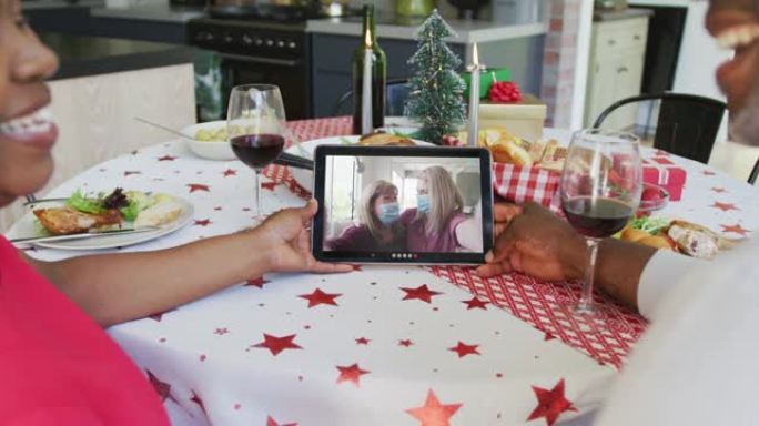 非裔美国人夫妇与葡萄酒使用平板电脑进行圣诞节视频通话，屏幕上有幸福的家庭