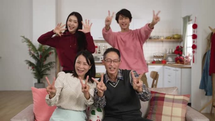 幸福的四口之家微笑着对着镜头，拇指和胜利的手势，在一个装饰着中国新年装饰的现代房子内部拍摄照片