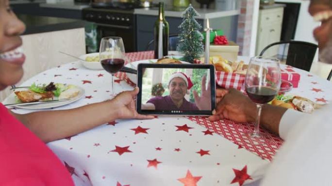 微笑的非洲裔美国夫妇使用平板电脑与屏幕上的快乐男人进行圣诞节视频通话