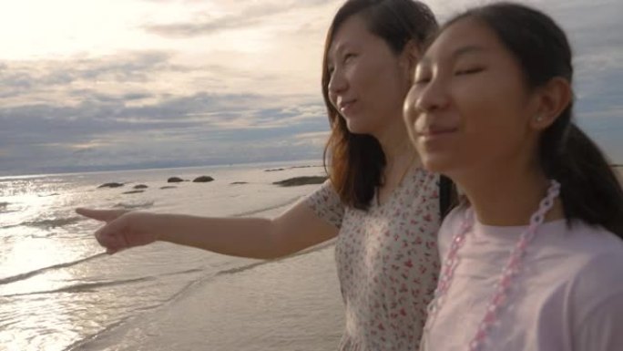 快乐的亚洲母亲和女儿一起看着海滩上的景色，以及日出背景、生活方式的概念。