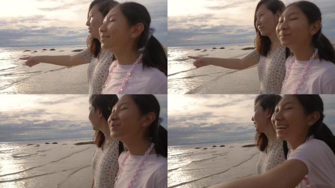 快乐的亚洲母亲和女儿一起看着海滩上的景色，以及日出背景、生活方式的概念。