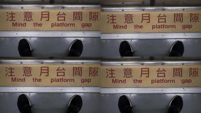 一个人站在火车车厢的门前。特写脚。中文意思是注意平台的差距。火车在行驶，相机摇晃。看过去。