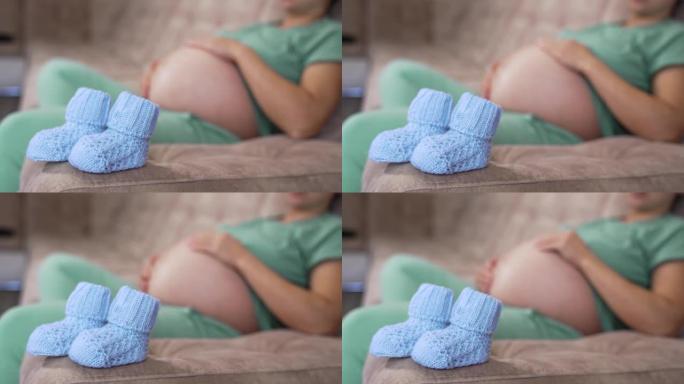 漂亮的针织袜子，适合未来的宝宝。准妈妈躺在沙发上的模糊背景上的新蓝色袜子。怀孕时间。