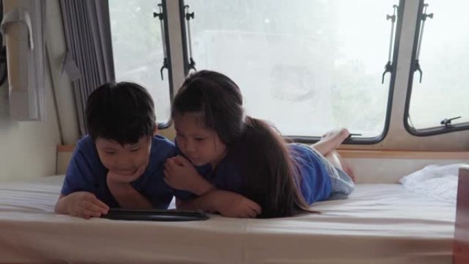 亚洲兄弟姐妹在大篷车上使用平板电脑。当他们在夏日躺在前面时。房车假日旅行