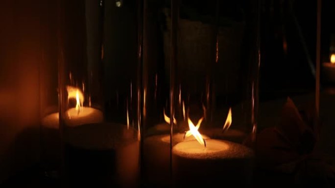 在黑暗中的玻璃花瓶里燃烧白色蜡烛。浪漫的夜晚概念。漂亮的玻璃花瓶，带装饰和燃烧的蜡烛