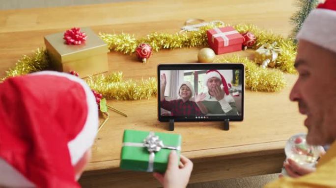 戴着圣诞老人帽子的高加索父子使用平板电脑与家人在屏幕上进行圣诞节视频通话