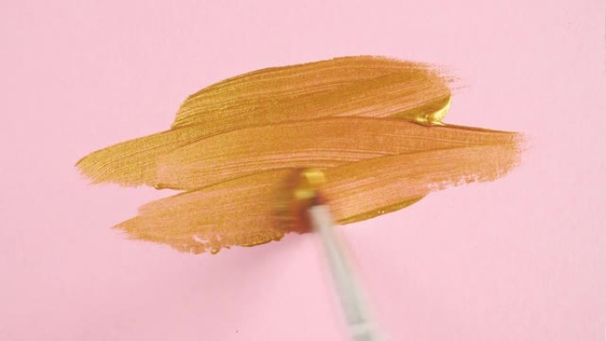 金色画笔的抽象笔触孤立地应用在粉红色背景上。金色油漆涂抹纹理。金色闪闪发光的纹理艺术插图。化妆品涂片