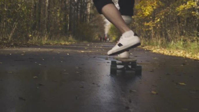 一个拥有金属仿生假肢的年轻人正在秋天的森林里骑滑板。一条人造腿推开滑板上的沥青