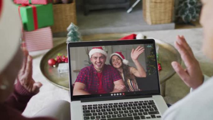 多元化的资深女性朋友挥舞着并使用笔记本电脑与屏幕上的情侣进行圣诞节视频通话