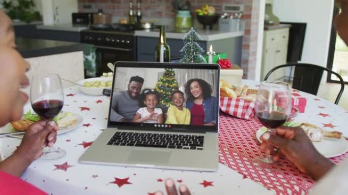 非裔美国人夫妇与葡萄酒使用笔记本电脑进行圣诞节视频通话，屏幕上有幸福的家庭