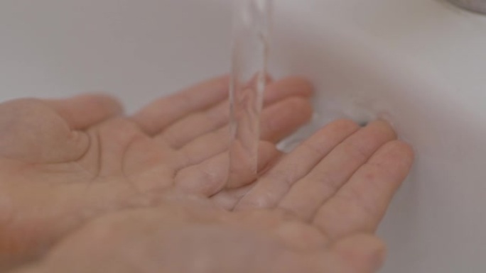 家里浴室里的小女孩触摸自来水检查温度。慢动作。人类手在自来水中的纯水流下的特写镜头。儿童手掌在水流下