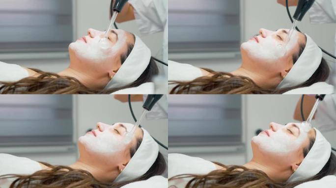 在医疗办公室的右脸颊和头顶使用高频d'arsonval装置的女性-客户用涂抹的面霜和专家躺在脸上
