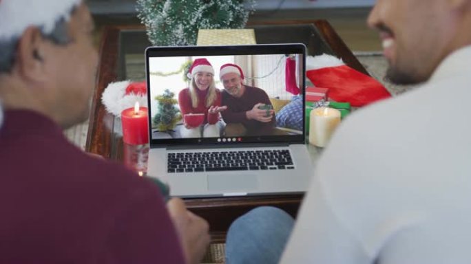 带有圣诞老人帽子的混血儿父子使用笔记本电脑进行圣诞节视频通话，屏幕上有情侣