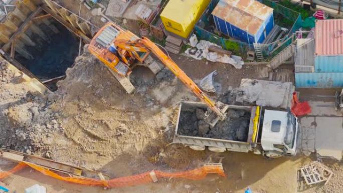 挖掘机在建筑工地挖一个基坑，并将土壤装载到卡车的后部，鸟瞰图