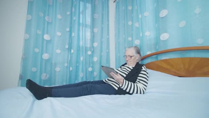 老白发女子通过躺在床上的平板电脑阅读新闻
