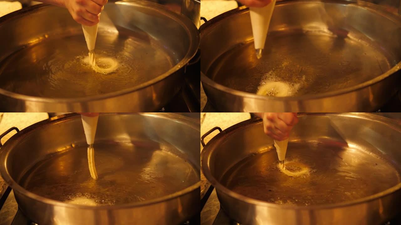 厨师的特写镜头将面团从糕点袋中挤出到油中。