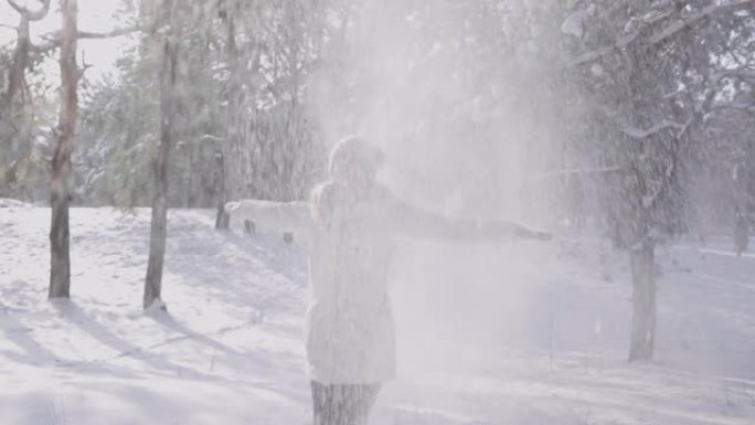 快乐的微笑女孩在飘落的雪中欢欣鼓舞。白色的雪花在太阳的光芒中闪闪发光。从白雪覆盖的树上落下的雪。美丽