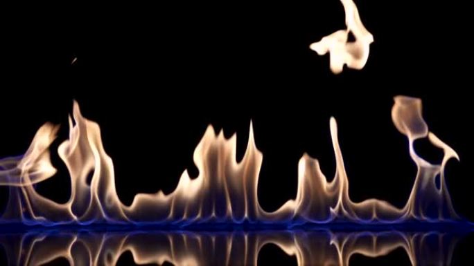 黑色反射背景下易燃液体或汽油的闪光和火焰条纹。一场大火，燃烧的舌头在蓝光中燃烧，以慢动作关闭。火焰