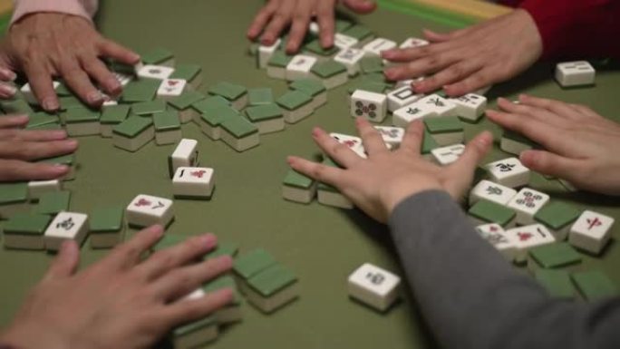 用绿色布在桌子上混合麻将牌的手的特写视图。农历新年概念期间的传统亚洲赌博游戏