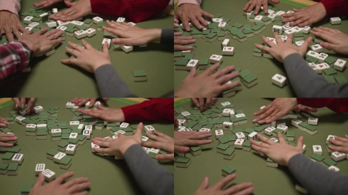 用绿色布在桌子上混合麻将牌的手的特写视图。农历新年概念期间的传统亚洲赌博游戏