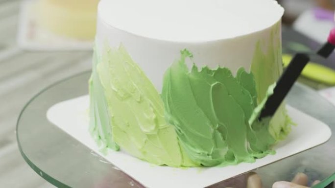 特写，厨师正在蛋糕周围撒上柔和的绿色奶油。