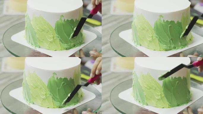 特写，厨师正在蛋糕周围撒上柔和的绿色奶油。