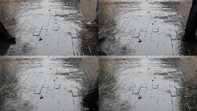 人们穿着靴子的脚在雨中行走。秋天城市街道上的大雨。秋天的树叶躺在下雨的路上