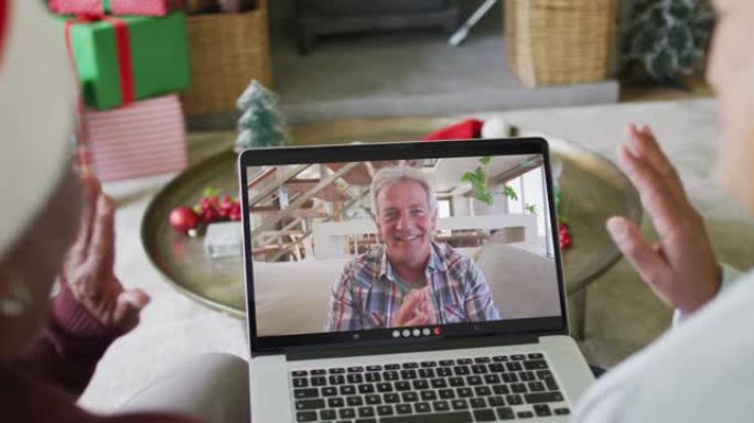 多元化的资深女性朋友使用笔记本电脑与屏幕上的快乐男人进行圣诞节视频通话