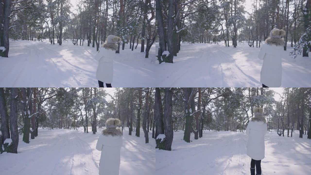 穿着冬季羽绒服的女孩在白雪皑皑的冬季森林中漫步。年轻女子高兴地微笑着环顾四周。森林里有很多雪。下雪的