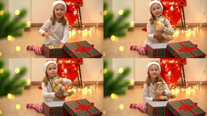 戴着红色圣诞老人帽子的快乐小孩在圣诞树旁边打开带有礼物玩具老虎的盒子。中国十二生肖新年的象征