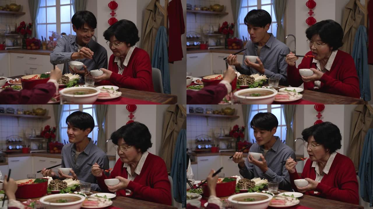 微笑的亚洲成年儿子在农历新年前夜在家里的饭厅里一起吃团圆饭时，给年长者母亲送饭