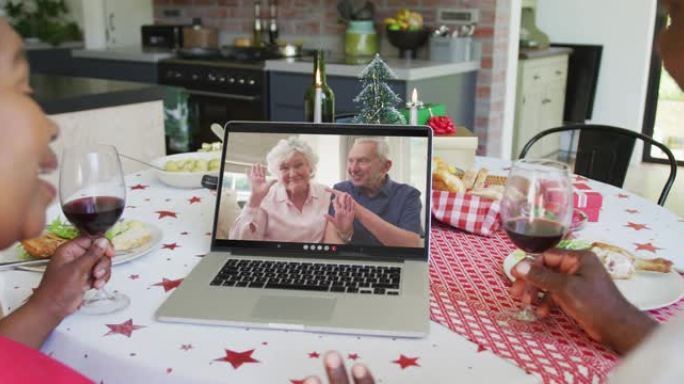非裔美国人夫妇与葡萄酒使用笔记本电脑进行圣诞节视频通话与屏幕上的幸福夫妇