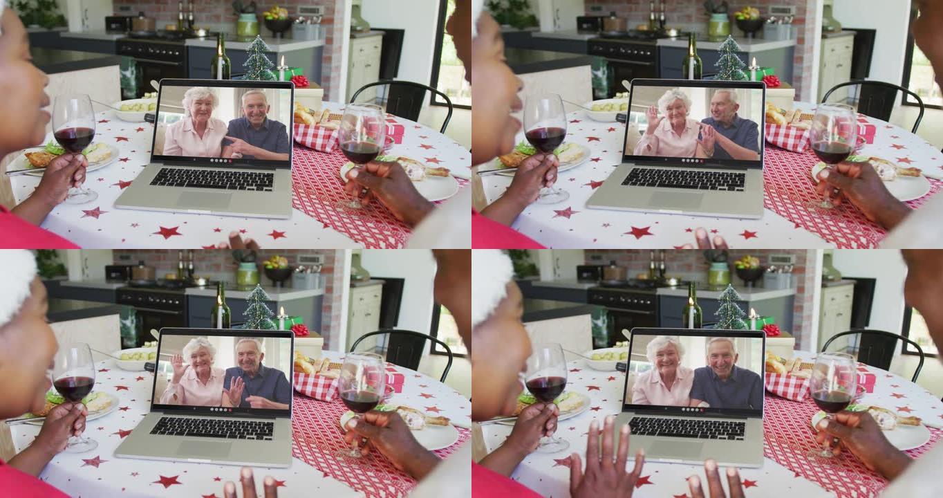 非裔美国人夫妇与葡萄酒使用笔记本电脑进行圣诞节视频通话与屏幕上的幸福夫妇