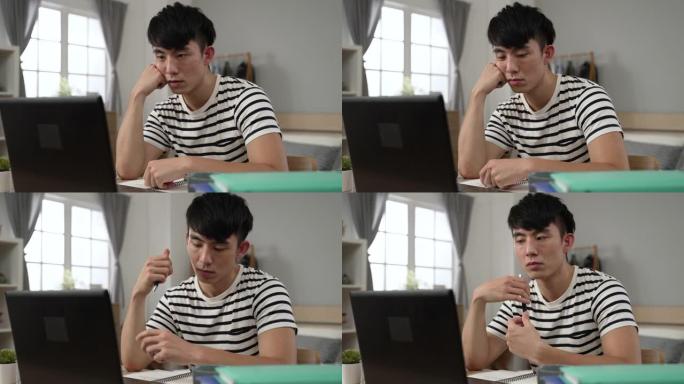 无聊的亚洲成年学生在家学习时，在锁定期间在卧室的计算机上学习在线课程时，正在支撑着脸并玩笔。