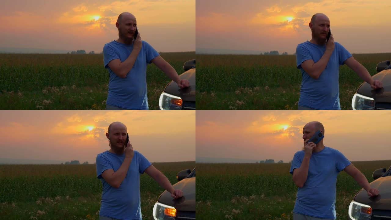 日落时分，一个留着胡须的秃头男人站在玉米田旁路边的一辆破车旁，打电话给技术服务或拖车。汽车在道路上出