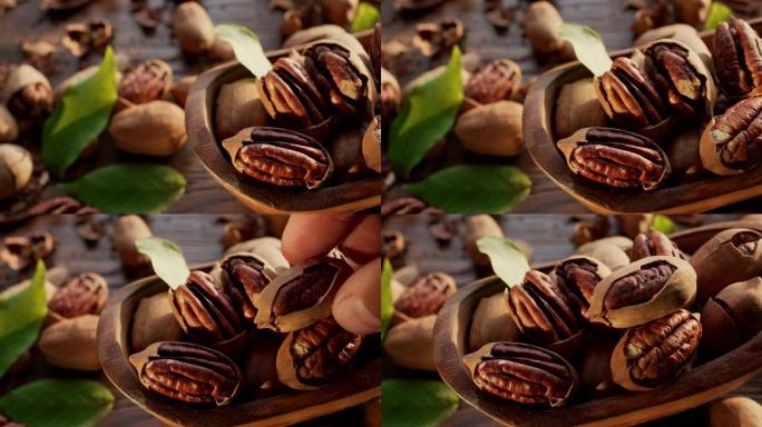 山核桃在一个带有山核桃叶和坚果壳的木碗中-特写视频，相机慢动作。手拿了一个山核桃坚果。