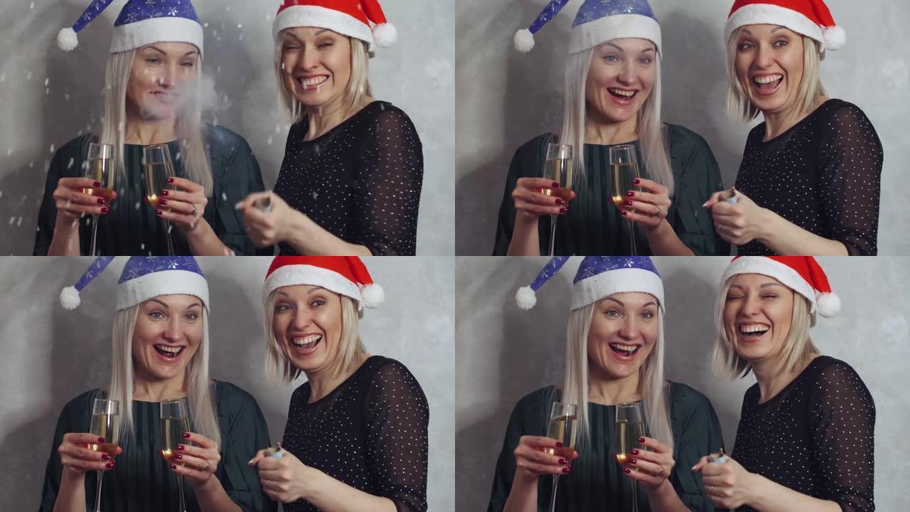 两个非常情绪化的女孩，手里拿着一杯香槟，穿着新年的帽子，炸开一个拍板大笑，庆祝新年和圣诞快乐