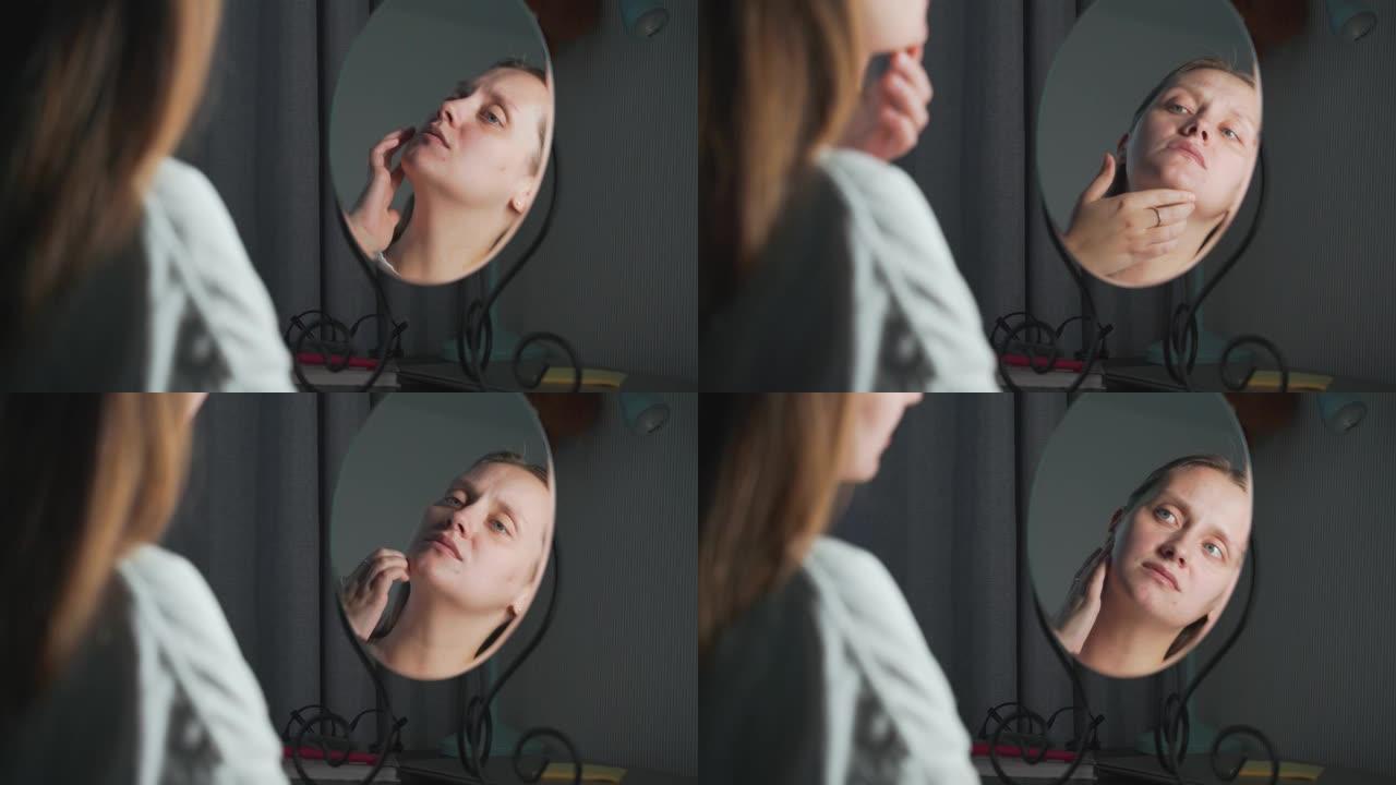 年轻女子看着镜子里的自己，检查她的脸的皮肤，感到不安。脸上有红肿和丘疹。这个女孩很沮丧。健康、美容