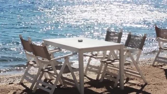 海滩餐厅和暑假概念。阳光下蓝色大海附近沙滩上的白色桌椅