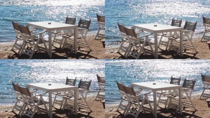 海滩餐厅和暑假概念。阳光下蓝色大海附近沙滩上的白色桌椅