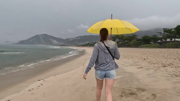 女子带黄伞在海边散步阴雨寒冷天