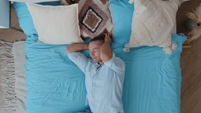 顶视图快乐有趣的高加索年轻人穿着睡衣跳跃，摔倒在床上弹跳，在卧室里在家放松享受。快乐的青春和现代生活
