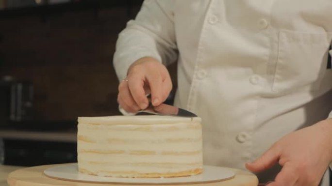 一位欧洲男士糕点厨师正在制作蛋糕准备表格。他用锋利的刀子将蛋糕上的奶油分清。创造甜蜜的甜点