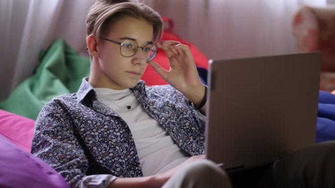 一个戴着眼镜的时尚少年看着笔记本电脑屏幕