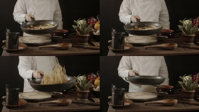 穿着白色制服的男厨师拿着煎锅，用新鲜蔬菜炒意大利面